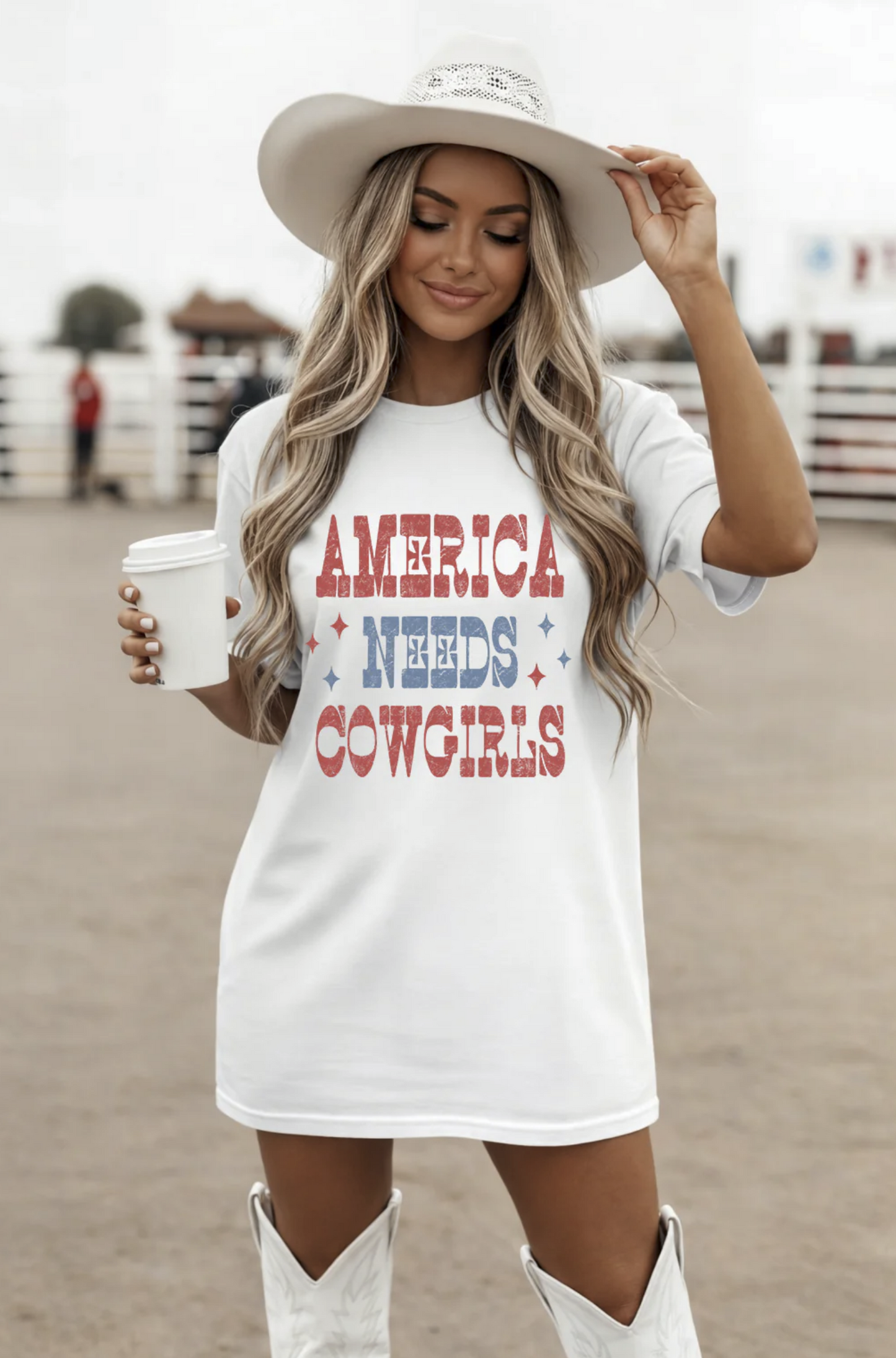 White t-shirt with red white and blue text reading “America Needs Cowgirls” worn with cowboy hat and boots
