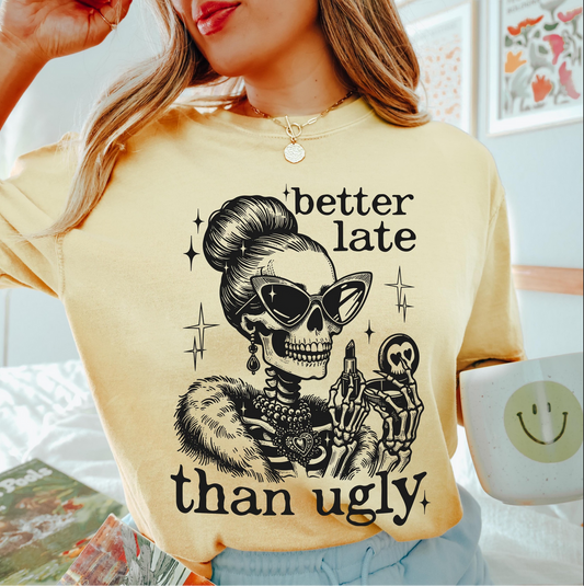 Light yellow Better Late Than Ugly t-shirt with stylish skeleton in sunglasses and fur coat holding a compact mirror, worn by a woman holding a smiley mug.