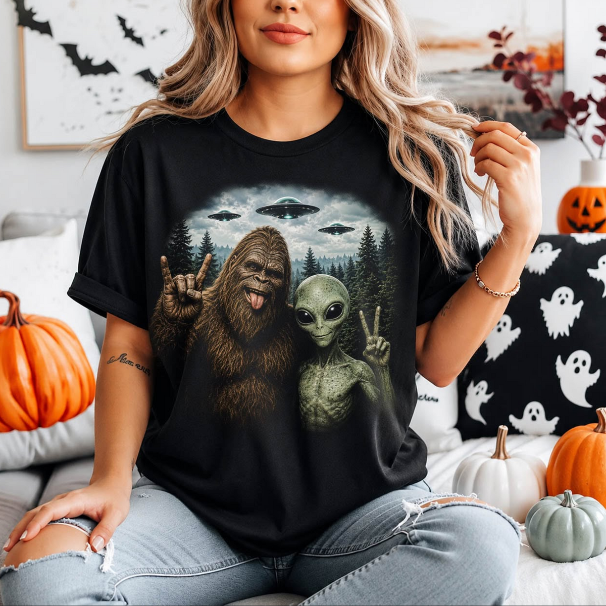 Model wearing a black graphic T-shirt featuring Bigfoot and a green alien posing in a forest beneath three flying UFOs.