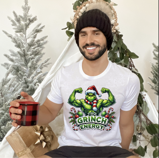 Man wearing a white Christmas T-shirt with a muscular green monster in a Santa hat flexing with the text Big Green Monster Energy.
