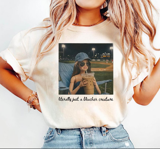 Cream graphic t-shirt featuring funny bleacher creature baseball mom design with iced coffee and game day sports theme