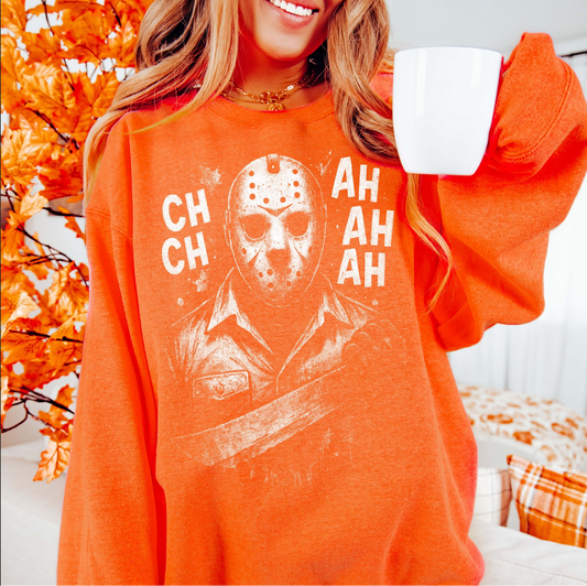 Orange Jason Mask Horror t shirt with distressed white graphic of Jason’s hockey mask and “CH CH AH AH” text, worn by a woman holding a coffee mug.