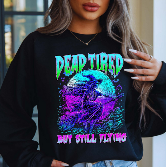 "Black sweatshirt with neon purple and blue skeleton witch flying on broomstick and text Dead Tired But Still Flying"