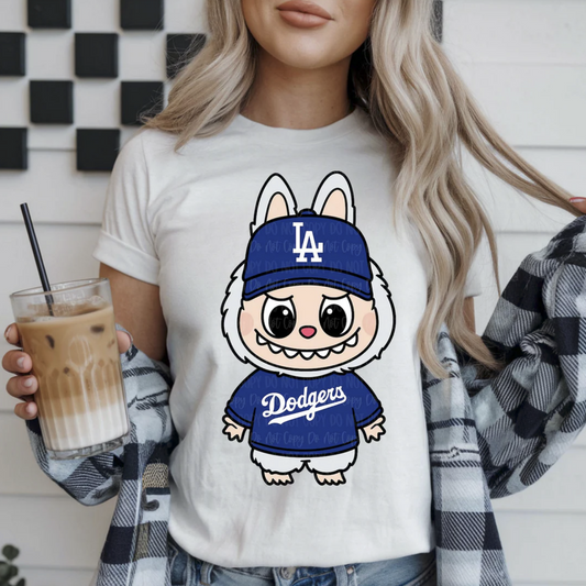 "White t-shirt featuring Labubu character wearing a blue Dodgers cap and jersey, cute anime-style baseball graphic."