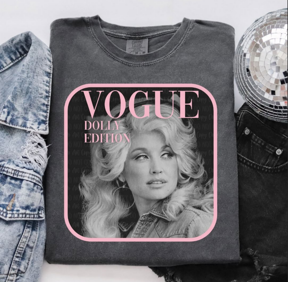 Folded washed-charcoal Comfort Colors T-shirt featuring a black-and-white Dolly Parton portrait with bright pink magazine-style lettering and border.