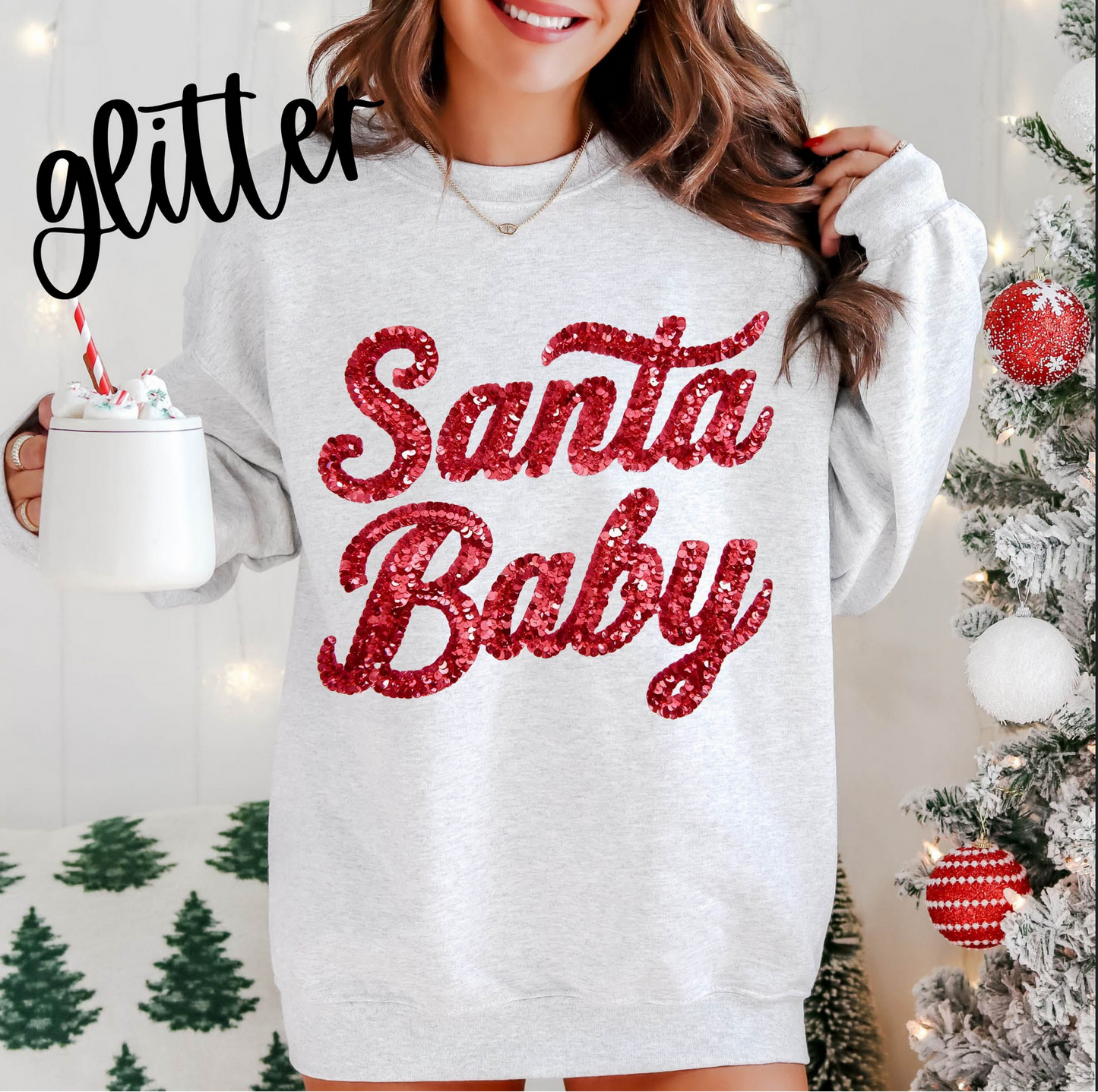 Light gray sweatshirt with red glitter-style ‘Santa Baby’ lettering, worn in a festive Christmas setting.