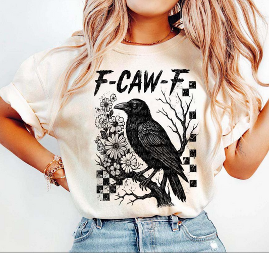Cream-colored t-shirt featuring a black raven perched on a branch with flowers and bold gothic text “F-CAW-F.”