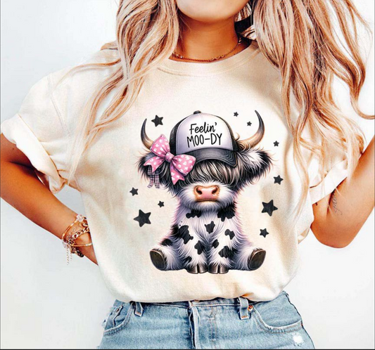 Feelin Moo-dy cute cow graphic tee with bow and hat design on beige shirt
