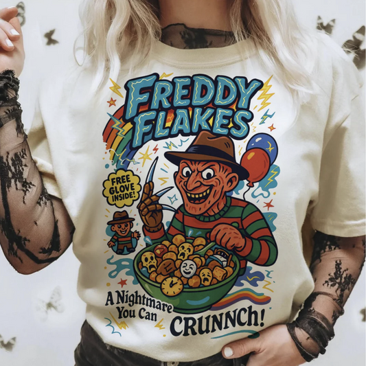 Beige t-shirt with colorful parody cereal box design featuring Freddy Krueger and text “Freddy Flakes – A Nightmare You Can Crunch!”