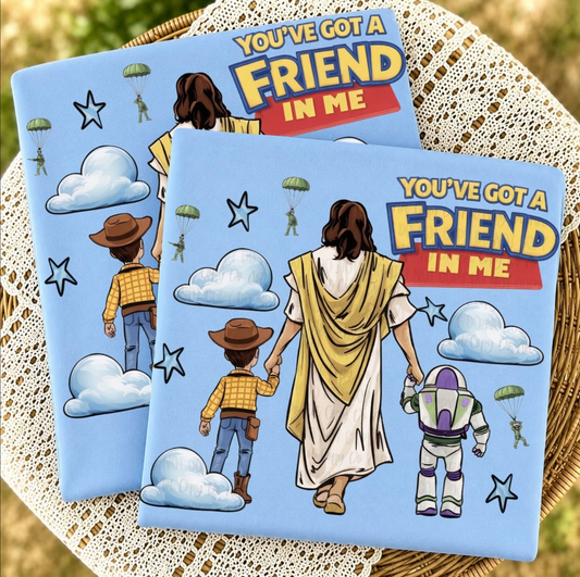 Christian graphic shirt featuring Jesus holding hands with a cowboy-inspired child and walking beside a space ranger beneath the phrase "You've Got a Friend in Me" on a blue background.