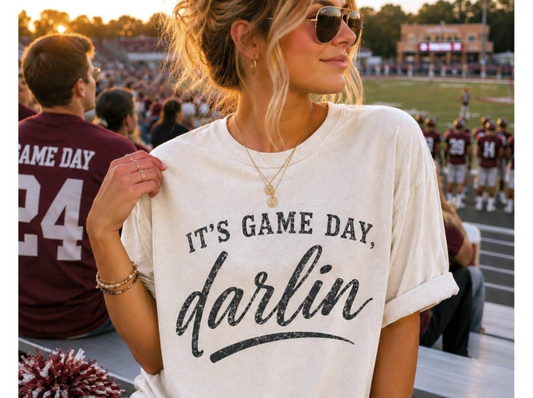 Model wearing a cream unisex graphic T-shirt with a distressed black design reading It’s Game Day, Darlin’.