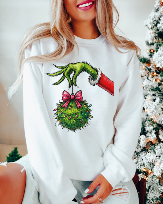 White sweatshirt with a green hand holding a fuzzy Christmas ornament with a pink bow