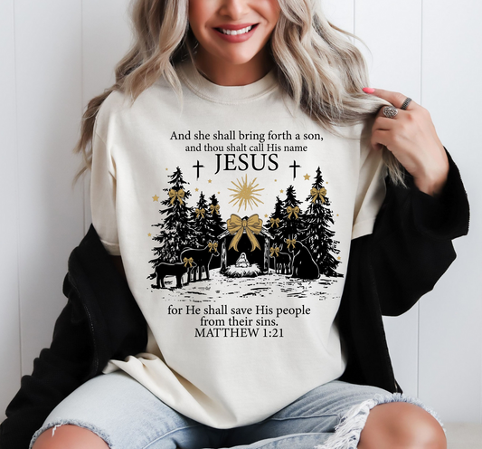 Cream sweatshirt with nativity scene, trees, star, and Matthew 1:21 Bible verse with Jesus’ name highlighted.