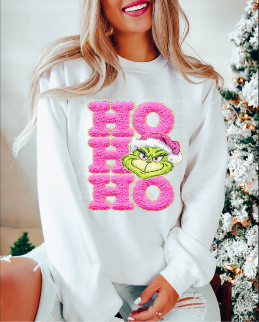 White sweatshirt with pink fuzzy ‘Ho Ho Ho’ lettering and a grumpy green Santa-faced character.