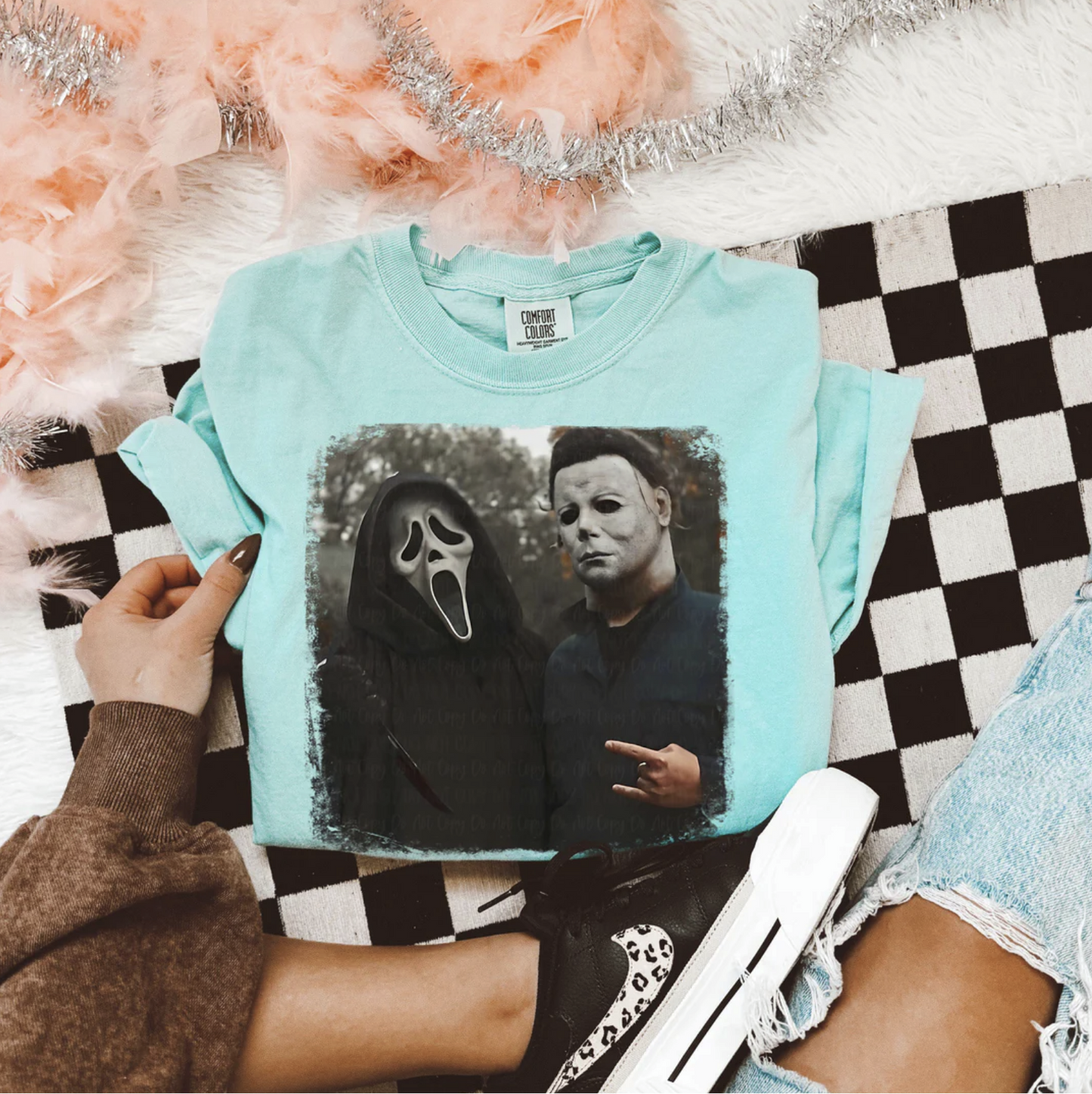 Light teal Scream & Michael Myers t-shirt with graphic of Ghostface and Michael Myers side by side, laid flat with casual outfit accessories.