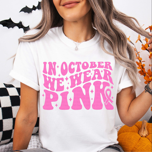 White Gildan Softstyle tee with bold pink retro lettering that reads ‘In October We Wear Pink’ with ribbon graphic, part of the $15 Tee Line