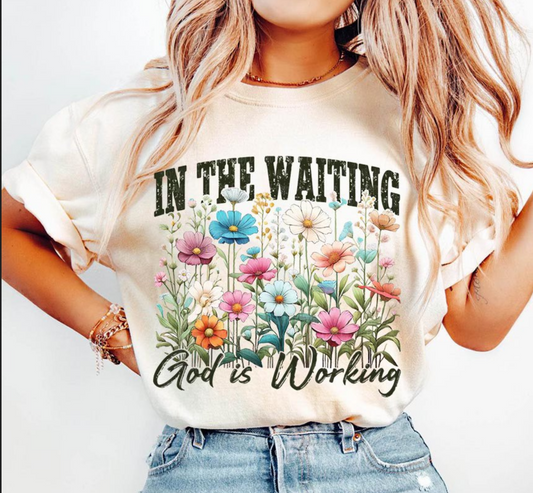 Woman wearing beige graphic t-shirt with colorful floral design and Christian quote “In The Waiting God Is Working” – inspirational faith shirt
