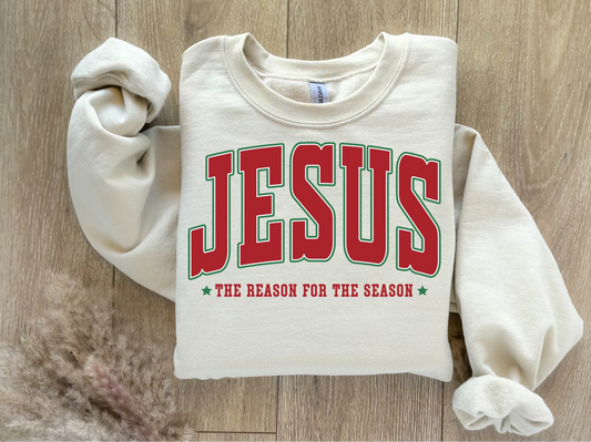 Cream sweatshirt with bold red JESUS lettering and The Reason for the Season text.

Christian holiday sweatshirt folded flat on wooden background.

Faith-based Christmas crewneck with red and green typography.

Cozy fleece sweatshirt featuring Jesus holiday design.