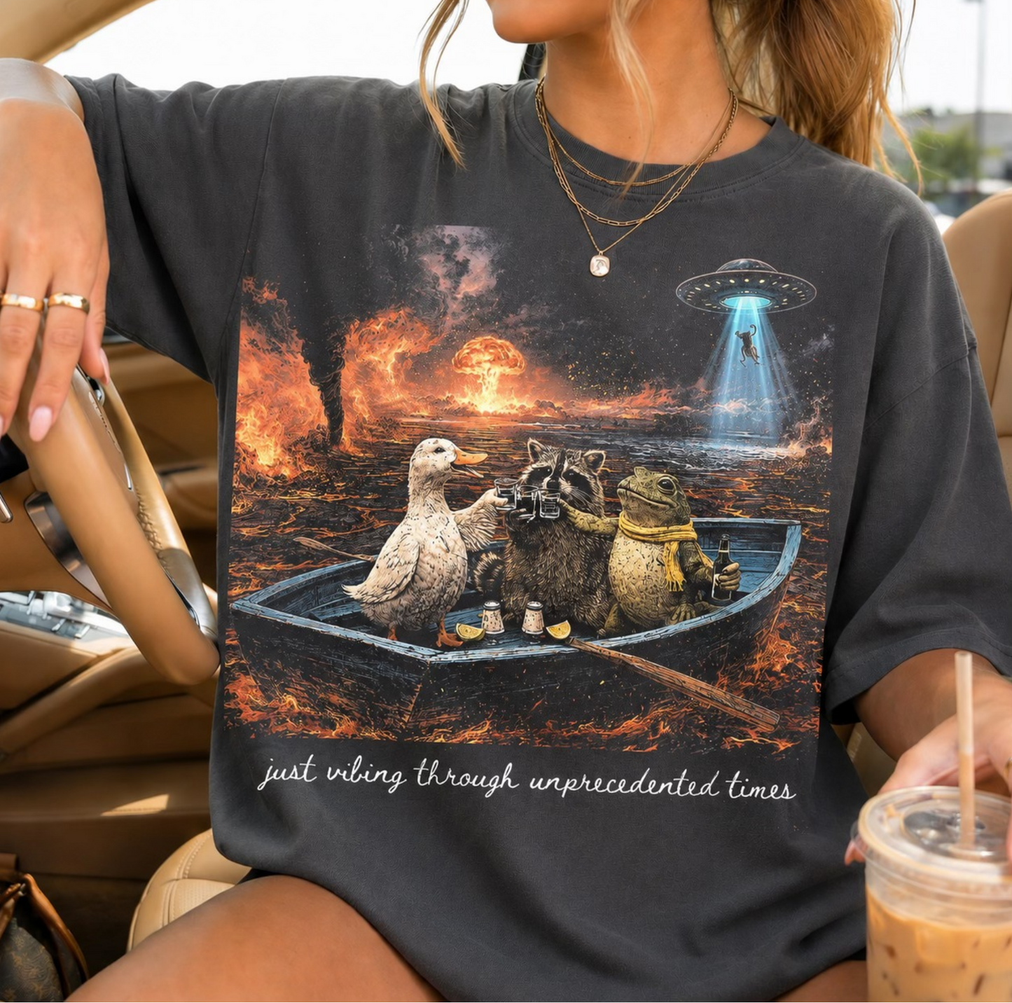 Dark graphic t-shirt with animals in a boat during a chaotic fiery scene and text “just vibing through unprecedented times”
