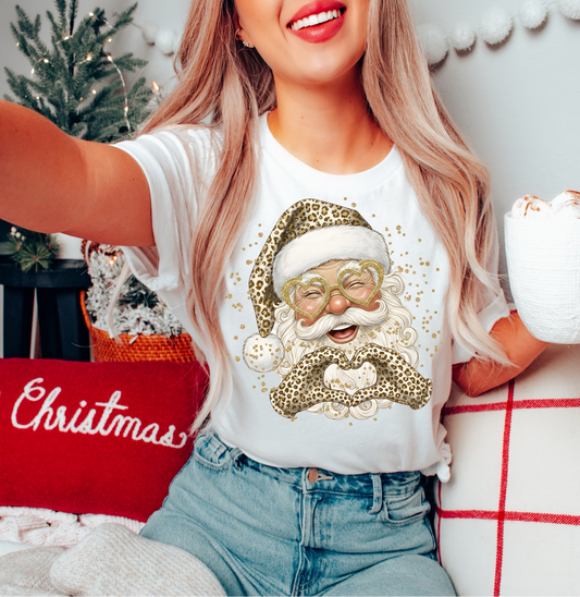Woman wearing white Leopard Santa graphic tee with festive mug

Trendy Christmas tee with leopard-print Santa design

Cozy holiday outfit featuring glam Santa shirt and jeans

White unisex Christmas tee — festive fashion for winter