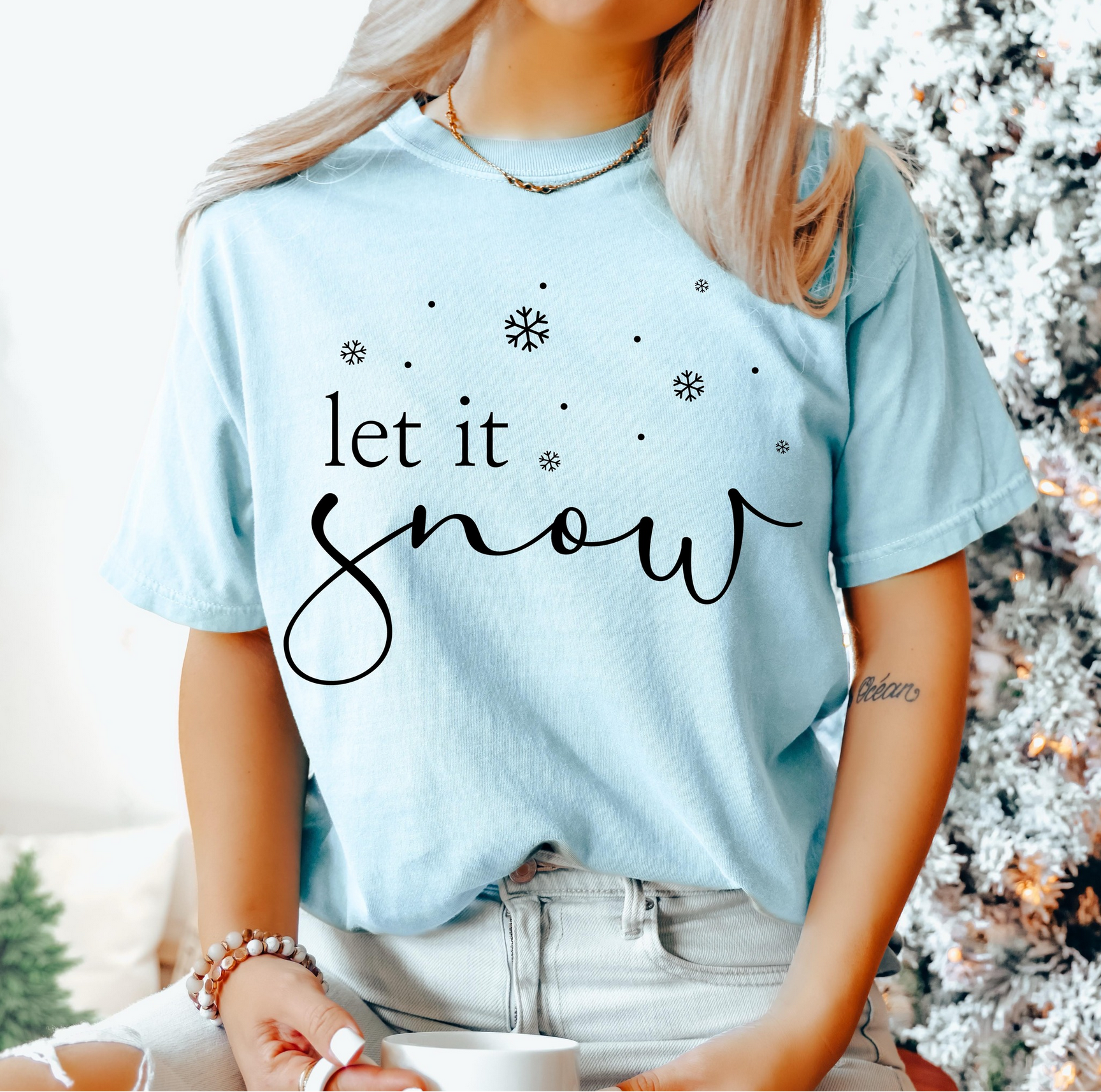 Light blue t-shirt with black script “let it snow” and scattered snowflakes.