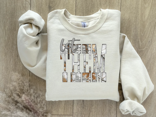 Neutral “Let Them” sweatshirt folded on wood surface with aesthetic block-letter design.

Cream crewneck with brown and tan block-letter quote “Let Them.”

Cozy neutral sweatshirt styled flat lay with soft minimal tones.

Inspirational quote sweater with retro graphic design.