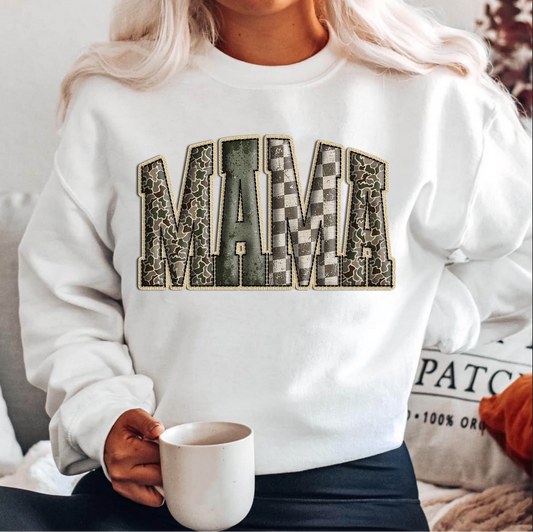 White sweatshirt with bold MAMA letters in textured patchwork patterns including checkered and floral designs.