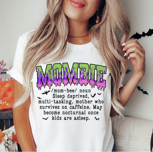 Woman wearing white “Mombie” graphic t-shirt with spooky purple and green text,
Funny Halloween mom shirt with “Mombie” definition printed on front, 
Casual unisex tee for moms, coffee lovers, and spooky season outfits, 
Close-up of “Mombie” text design on white graphic t-shirt