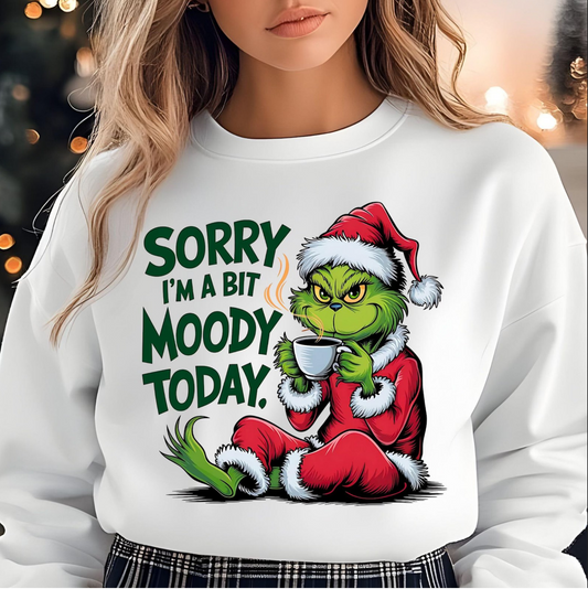 White sweatshirt with “Sorry I’m a Bit Moody Today” text and cartoon Grinch in Santa suit drinking coffee