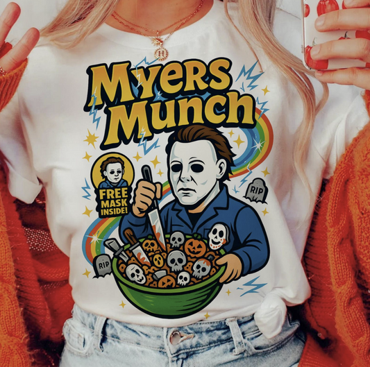 White t-shirt with cartoon Michael Myers holding spooky cereal bowl, text ‘Myers Munch’ – funny retro horror cereal box graphic tee