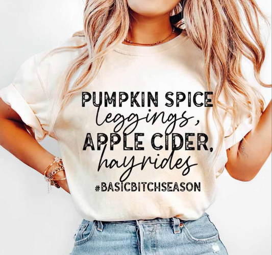 Beige graphic t-shirt with the words “Pumpkin Spice, Leggings, Apple Cider, Hayrides #BasicBitchSeason” in bold fall-inspired print.