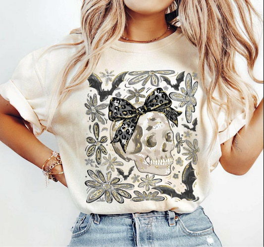 "Beige t-shirt with skull graphic, leopard bow, bats, and floral accents – gothic Halloween tee"