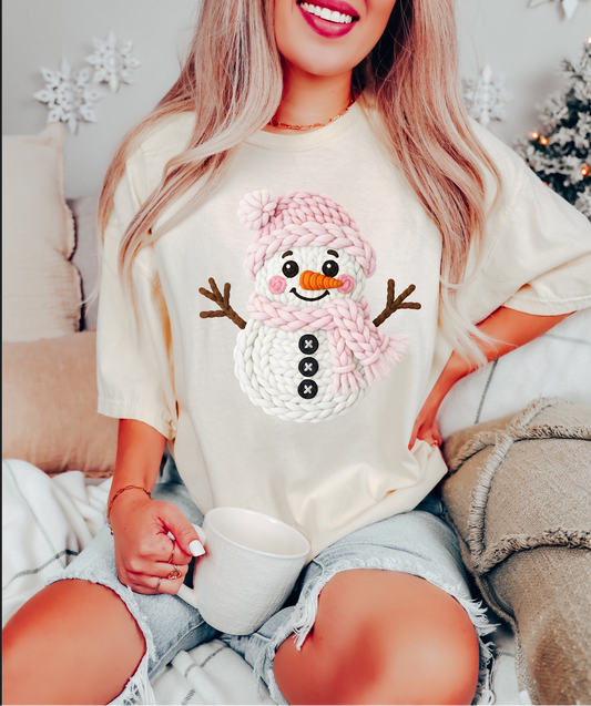 Woman wearing cozy crochet snowman tee with pink hat design

Neutral beige Christmas t-shirt with snowman print

Cute winter holiday graphic tee styled with shorts and mug

Soft unisex beige tee — cozy holiday outfit idea