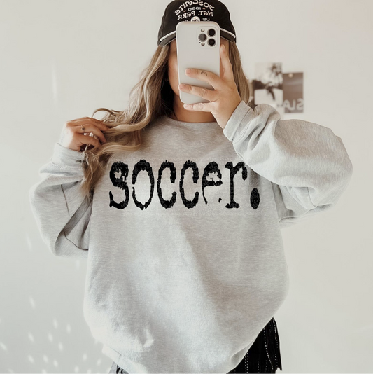 Gray unisex sweatshirt with bold distressed black text that reads ‘Soccer’ across the chest.