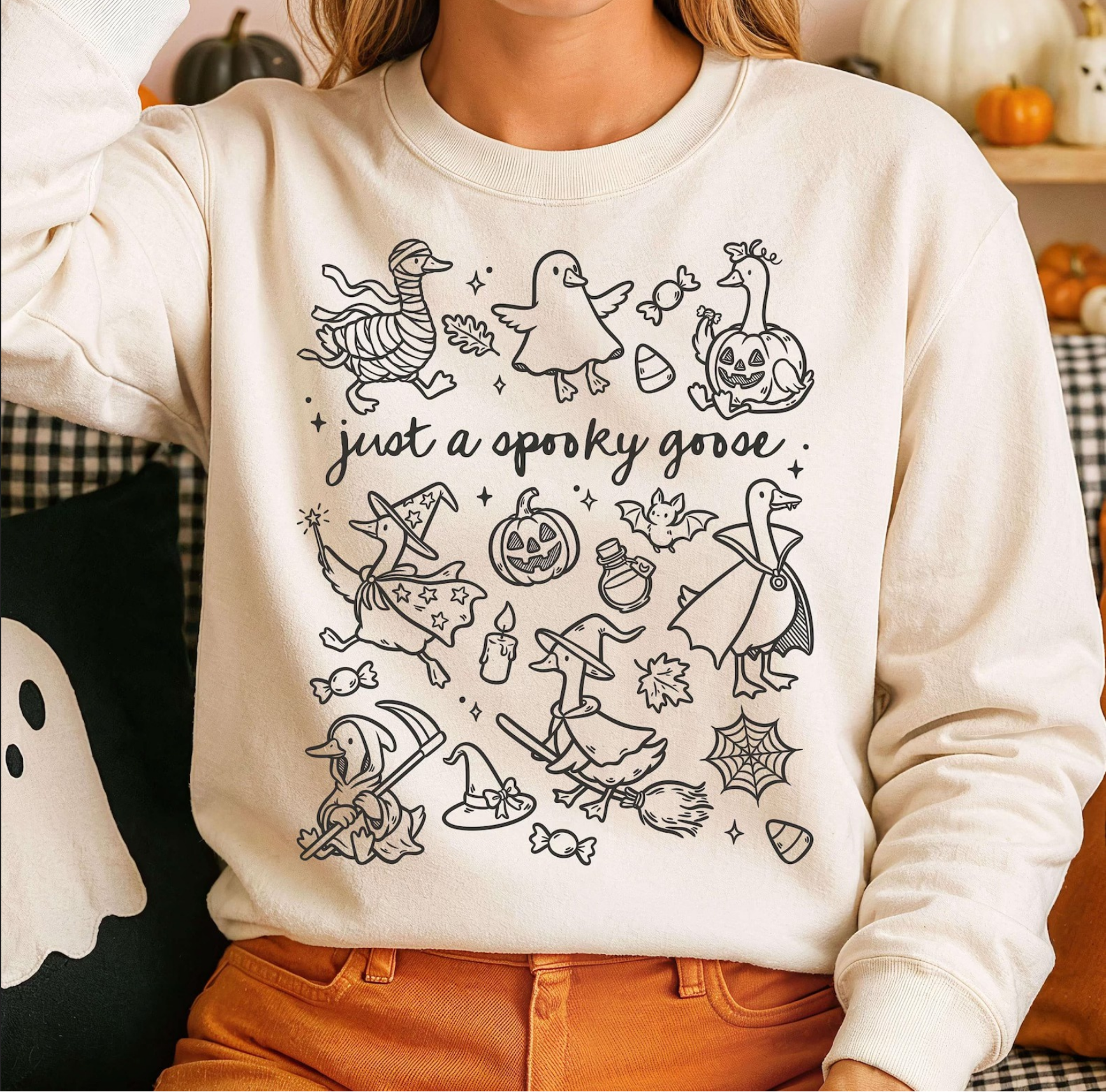 Cream crewneck sweatshirt with hand-drawn geese in Halloween costumes — ghost, pumpkin, mummy, witch — and the phrase “Just a Spooky Goose.”
