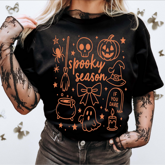 Black Spooky Season t-shirt with orange Halloween graphics including pumpkin, ghost, witch hat, broomstick, skull, and cauldron, worn with sheer spiderweb sleeves.