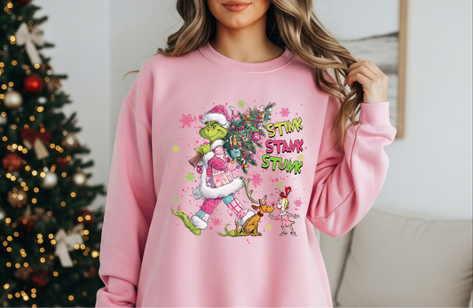 Pink sweatshirt featuring a grumpy green holiday creature carrying a decorated Christmas tree.

Close-up of pink holiday crewneck with funny green character graphic.

Cute festive sweatshirt styled for winter holiday decor.

Woman wearing pink holiday sweater with humorous Christmas artwork.