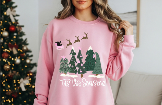 Woman wearing pink “’Tis the Season” sweatshirt by Christmas tree

Cozy holiday crewneck with reindeer and forest design

Pink Christmas sweatshirt with whimsical festive trees

Cute unisex holiday pullover styled for winter mornings