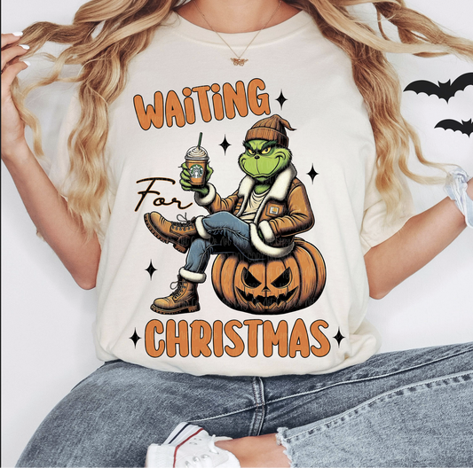 Beige t-shirt with Grinch-inspired character sitting on pumpkin holding holiday drink, text ‘Waiting for Christmas’ – festive graphic tee