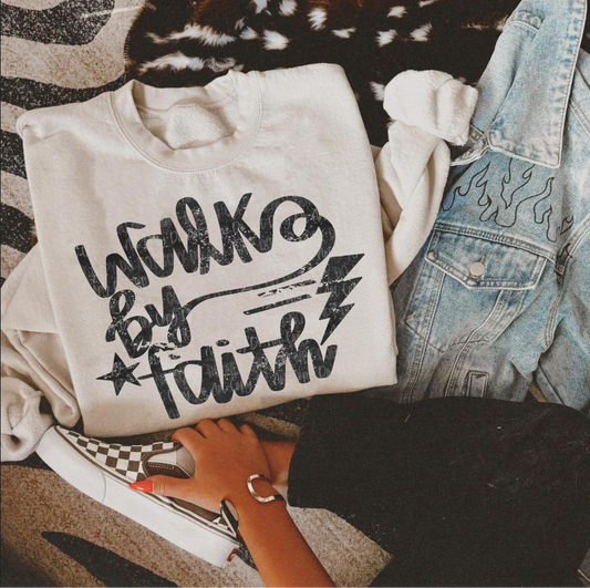 Cream Walk by Faith graphic sweatshirt with black lettering, star, and lightning bolt design, laid next to jeans and checkered sneakers.