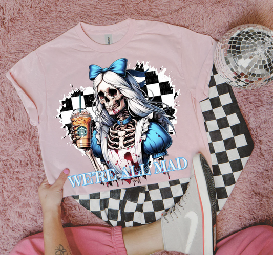 Pink tee with skeleton girl in blue bow holding iced coffee, text “We’re All Mad.”
Close-up of spooky gothic parody skeleton graphic on pink shirt.