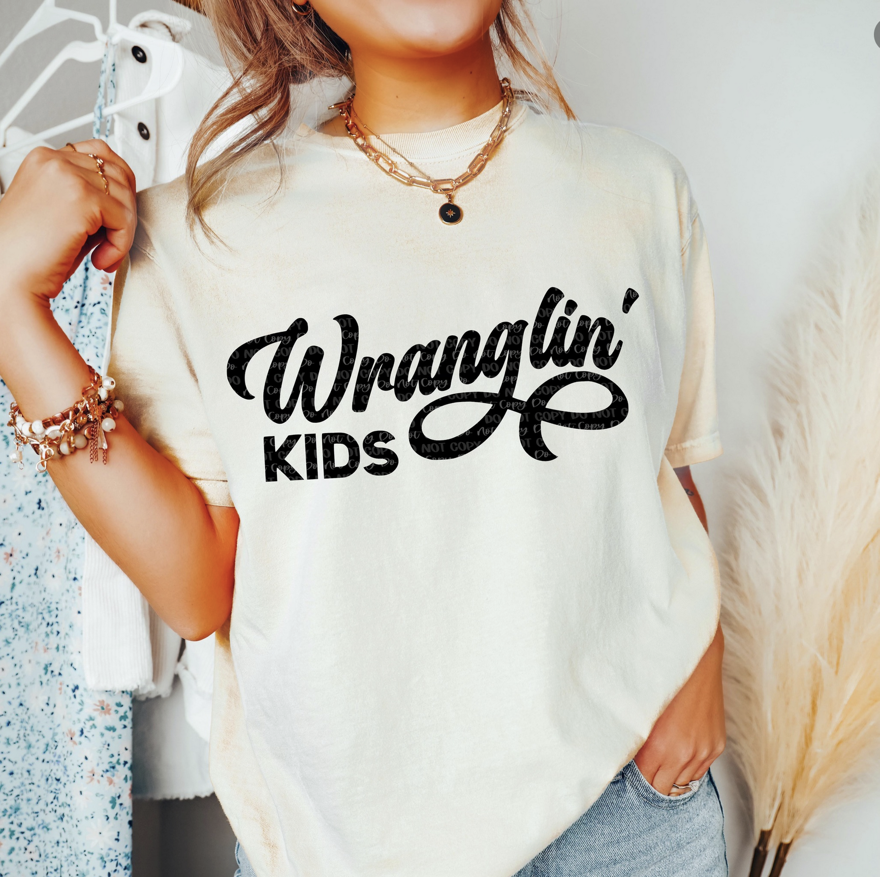 Beige t-shirt with black script text “Wranglin’ Kids” and rope graphic – funny western mom life tee